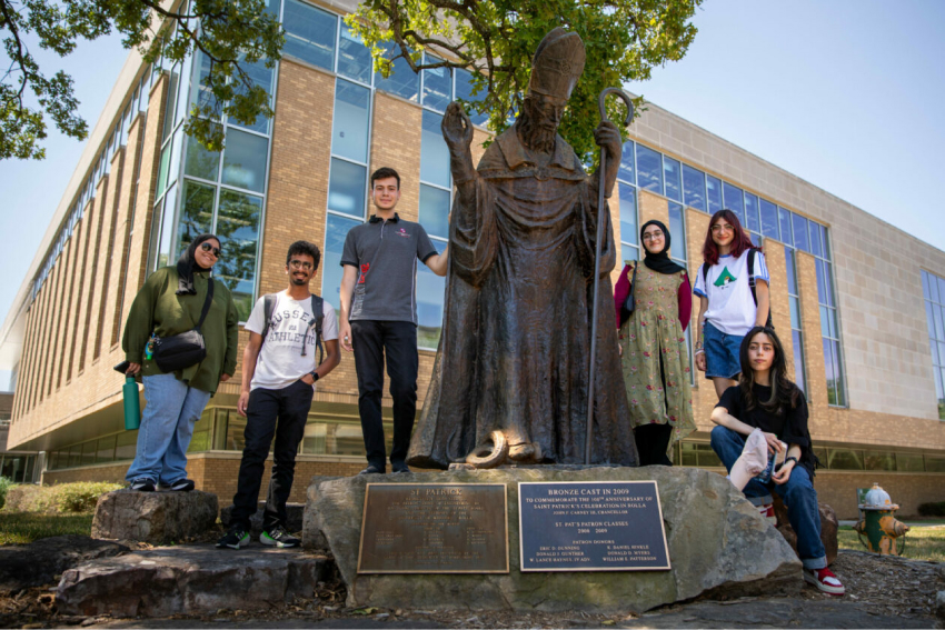 Six students visiting from Gulf University for Science and Technology in Kuwait stand next to the Saint Patrick statue on S&T's campus.